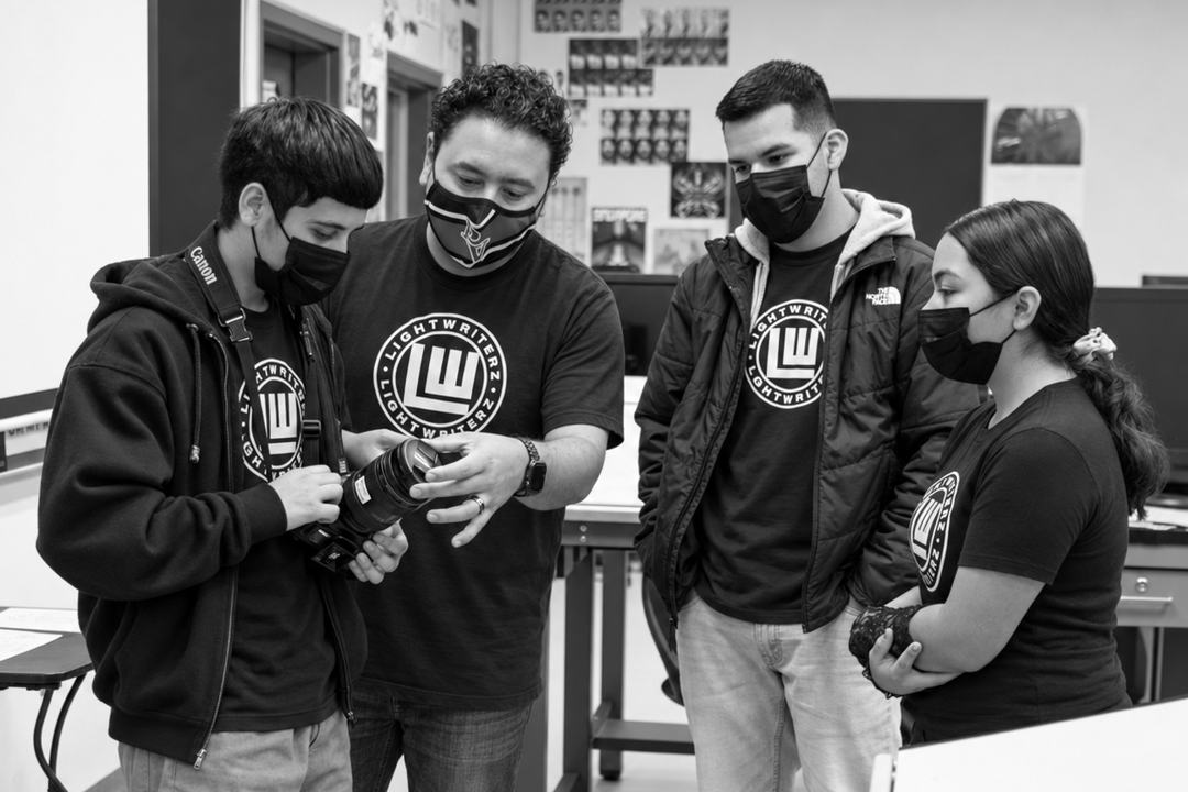 Light Writerz members wearing their earned LWZ shirts, reviewing an image on a camera in the classroom